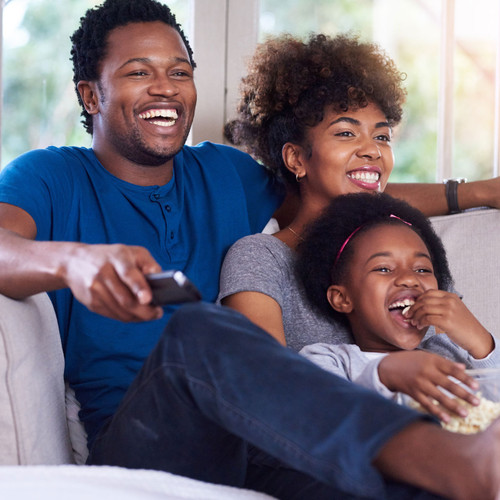 Man, woman and child sitting on a couch smiling while watching TV